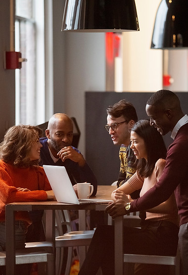Group of people sitting around a desk working together on a laptop computer